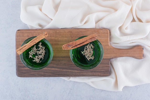 木のボードに置かれた、シナモンスティック添えの緑色のお茶のグラス二つ